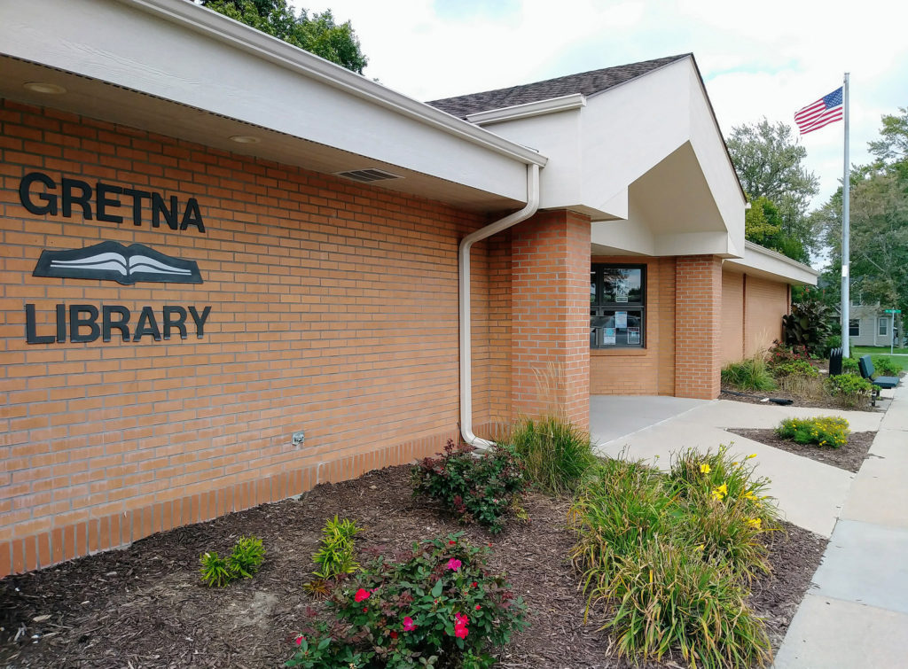 Exterior of the Gretna Public Library (Nebraska) Main Library building on South St. Features the brick building with library sign and native plants in the gardens.