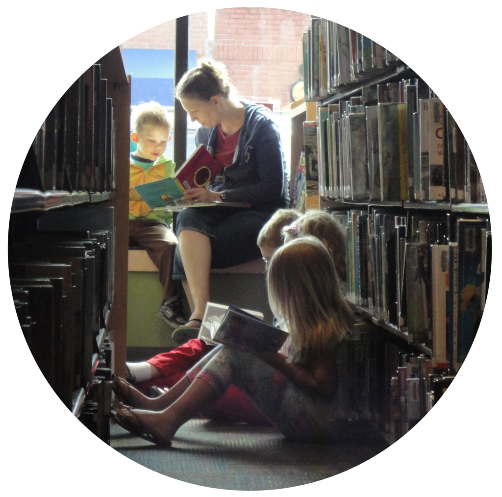 Photo in the shape of a circle featuring children and a mother reading down a library aisle.