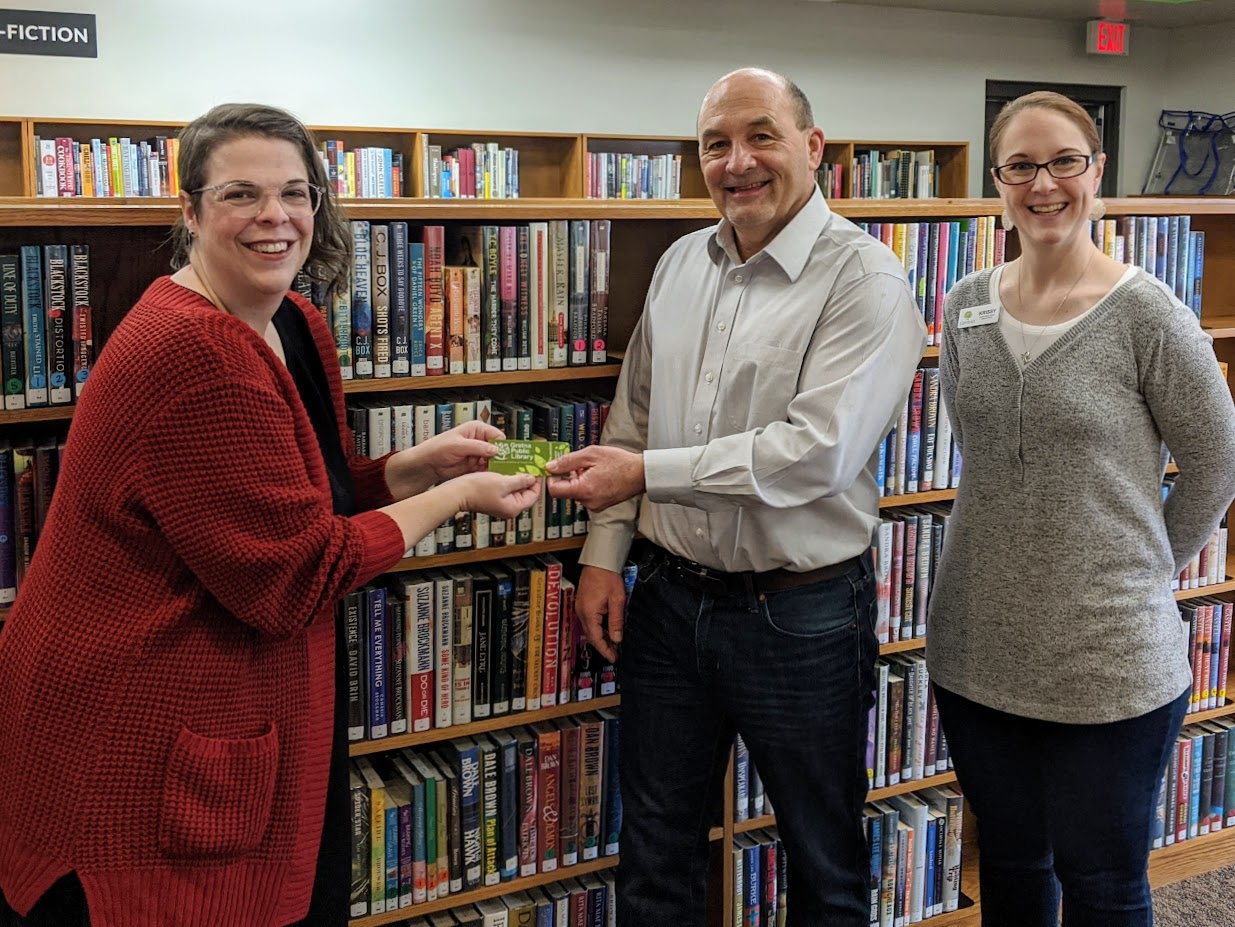 Librarian handing a new library card to the mayor of Gretna, Nebraska while the Library Director stands to the side.