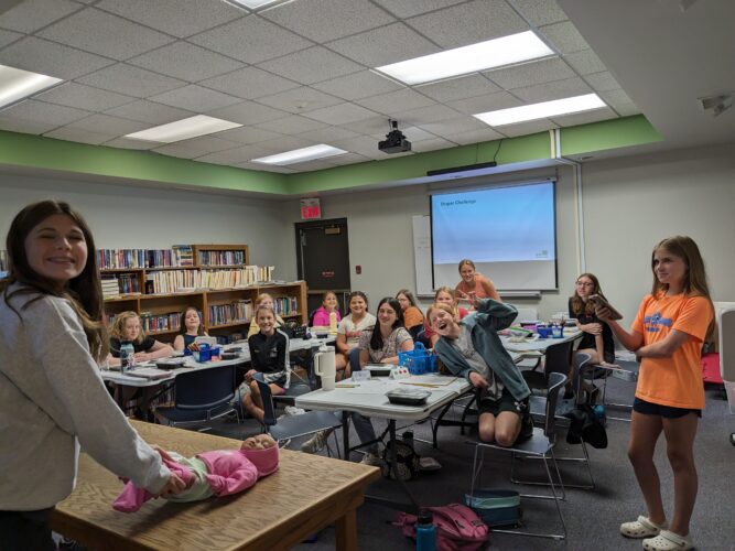 A babysitting class smiles at the camera. One of the students is changing a doll's diaper.