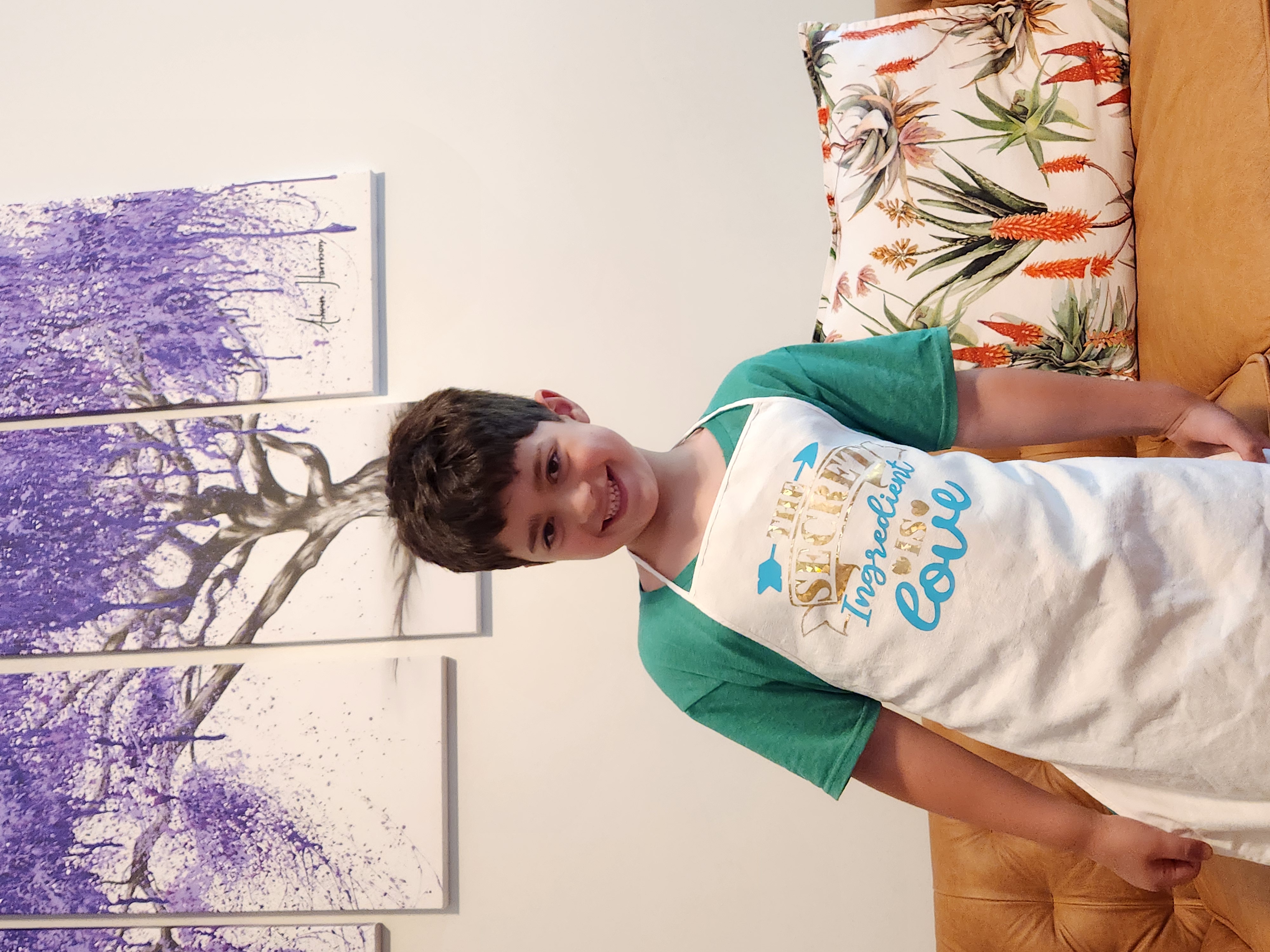 A young boy smiles in a white apron. The custom text reads "The secret ingredient is love."