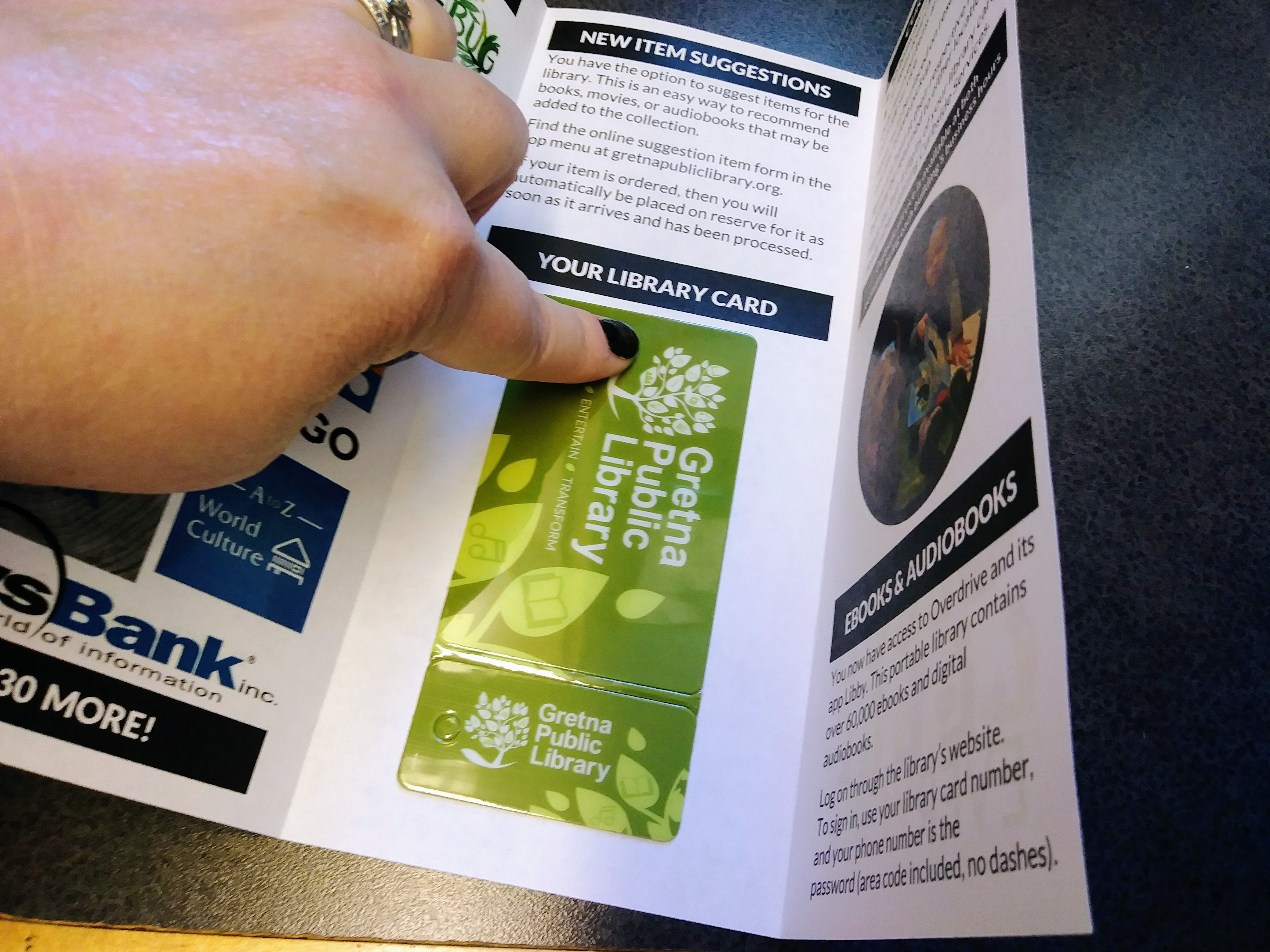 A finger pushes down on a Gretna Public Library card inside of a trifold brochure.