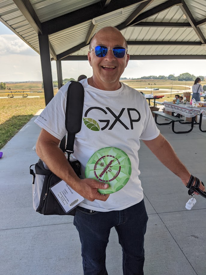 Image of the Mayor of Gretna at the opening for Gretna Crossing Park in September 2023. He is in sunglasses and excitedly showing off a green disc golf from a kit that patrons can borrow from the Gretna Public Library.