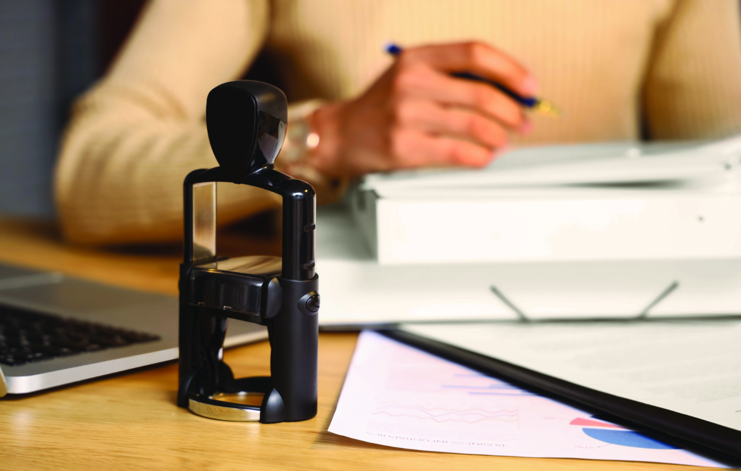 Closeup of a notary stamp with a woman and documents in the background.