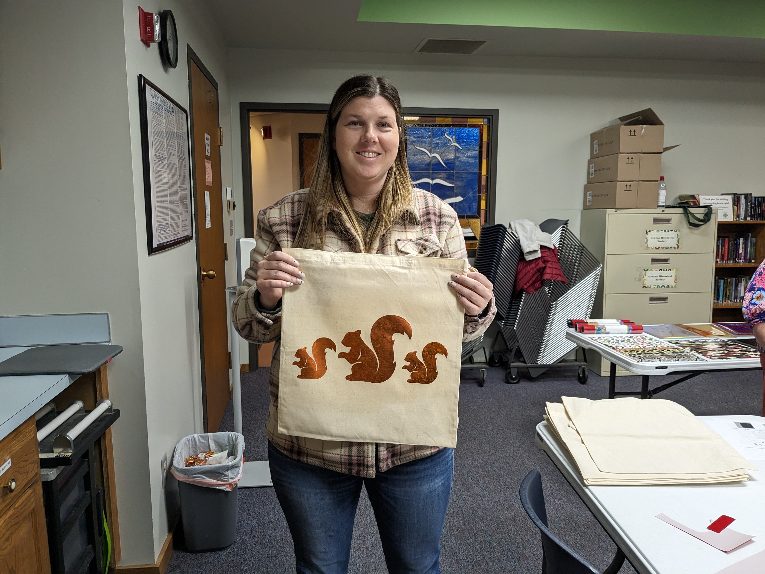 A woman smiles and holds a canvas bag with two small squirrels around one big one.