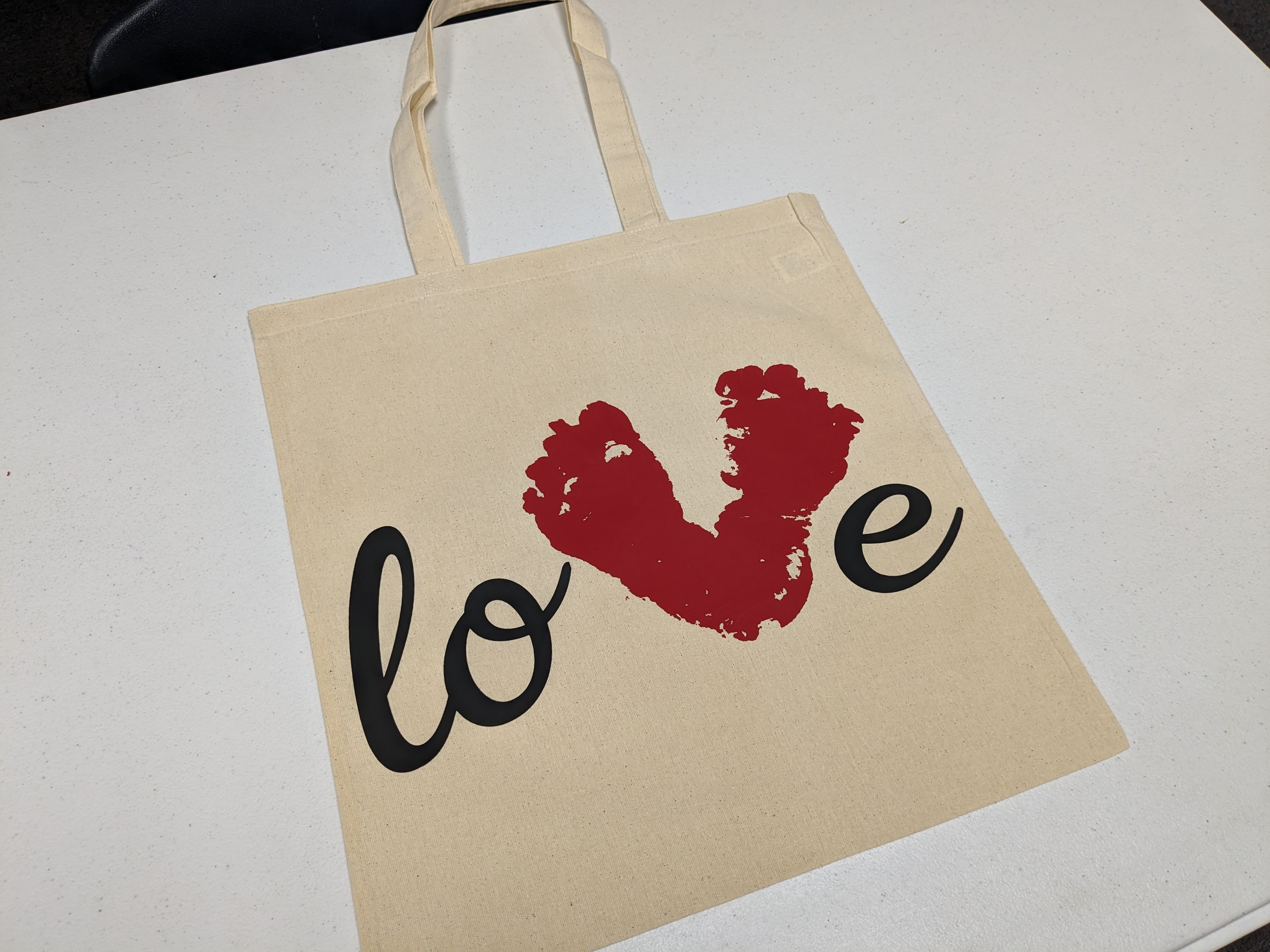 A canvas bag with the word "love" on it. The V is made with a baby's footprints.