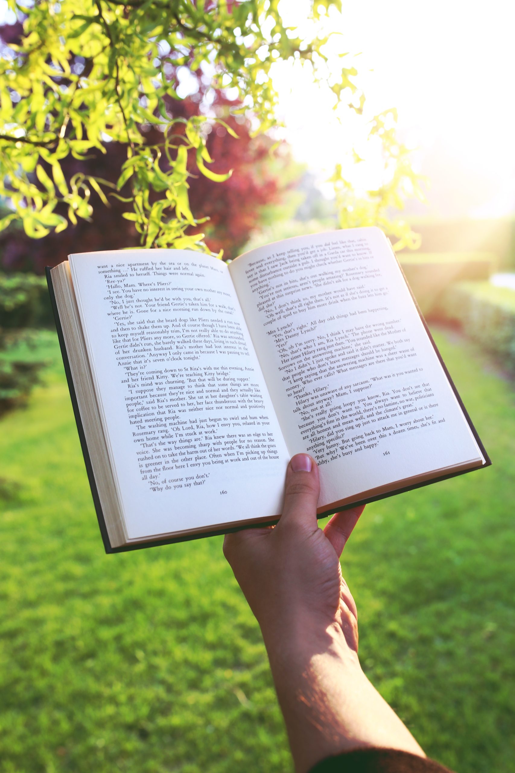 Hand holds an open book outdoors on a sunshiny day.